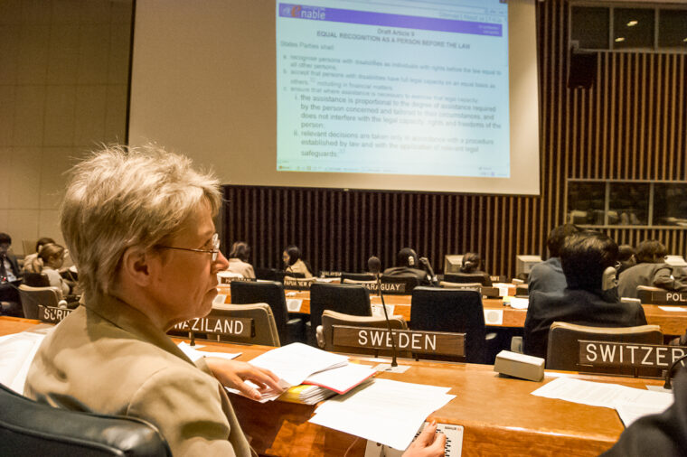 Foto på förhandlingssal i FN, Kerstin Jansson sitter bakom skylten ”SWEDEN”. På skärmen anas texten som är under förhandling.
